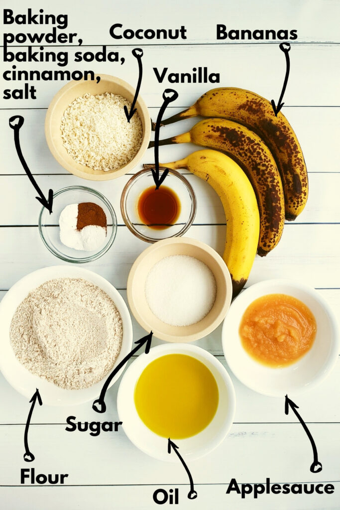 All the ingredients, including bananas, oil, applesauce, sugar, flour, coconut, vanilla, salt, cinnamon, baking powder, and baking soda.