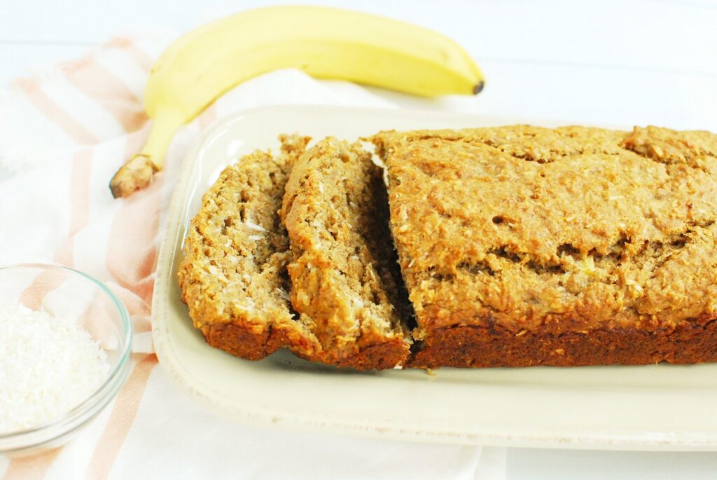 Sliced vegan coconut banana bread on a plate next to a napkin and a banana.