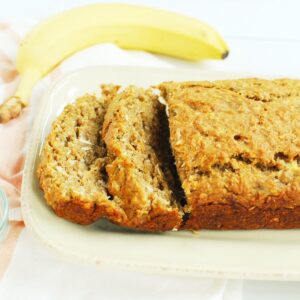 A loaf of vegan banana bread with a few slices cut into it on a plate.