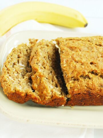 A loaf of vegan banana bread with a few slices cut into it on a plate.
