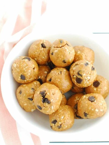 A white bowl full of healthy peanut butter cookie dough bites, next to a striped pink and white napkin.