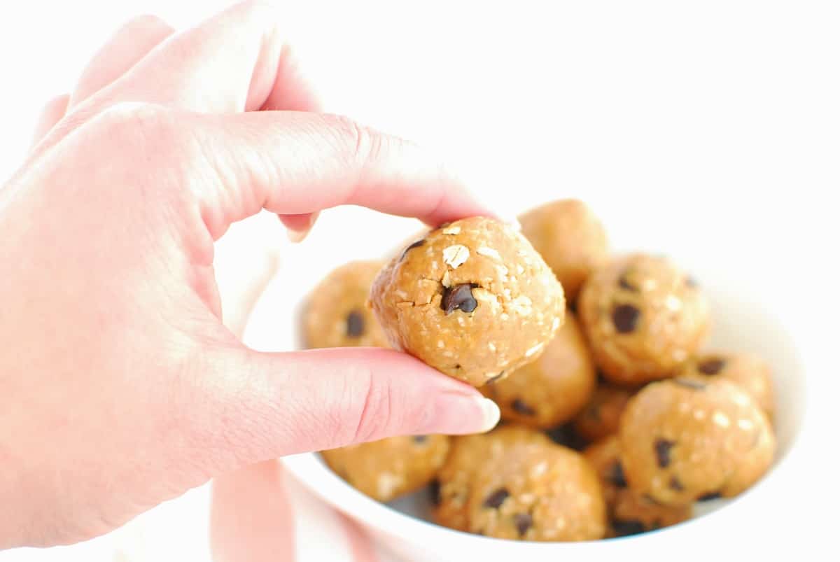 A woman's hand holding a peanut butter cookie dough ball.