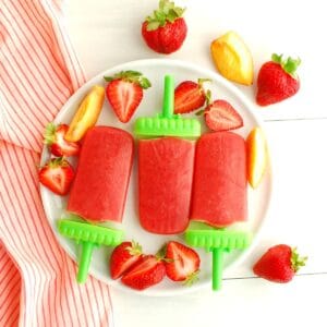 An overhead shot of three strawberry peach popsicles on a plate next to a napkin.