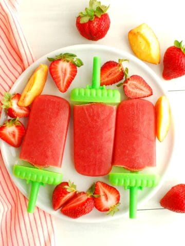 An overhead shot of three strawberry peach popsicles on a plate next to a napkin.