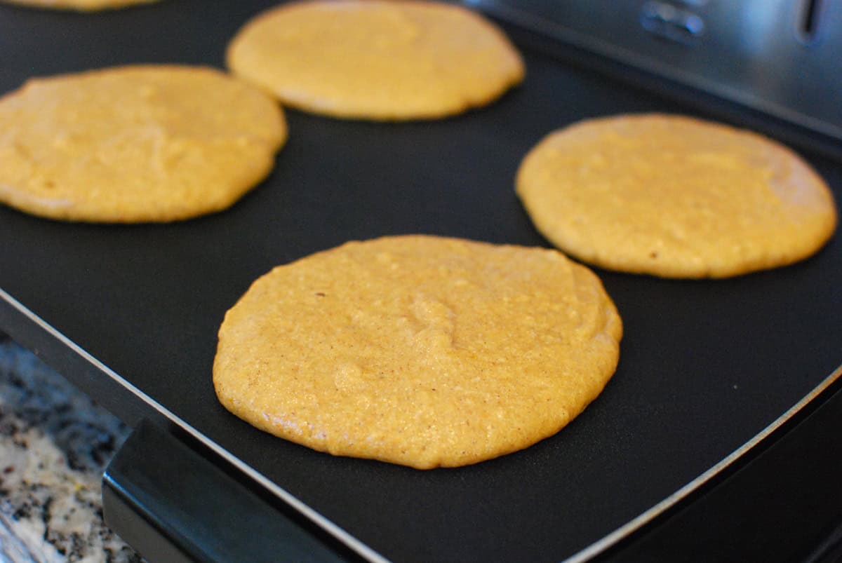 Pumpkin pancakes cooking on a griddle.
