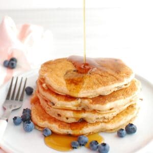 A stack of blueberry greek yogurt pancakes with maple syrup being drizzled on top.