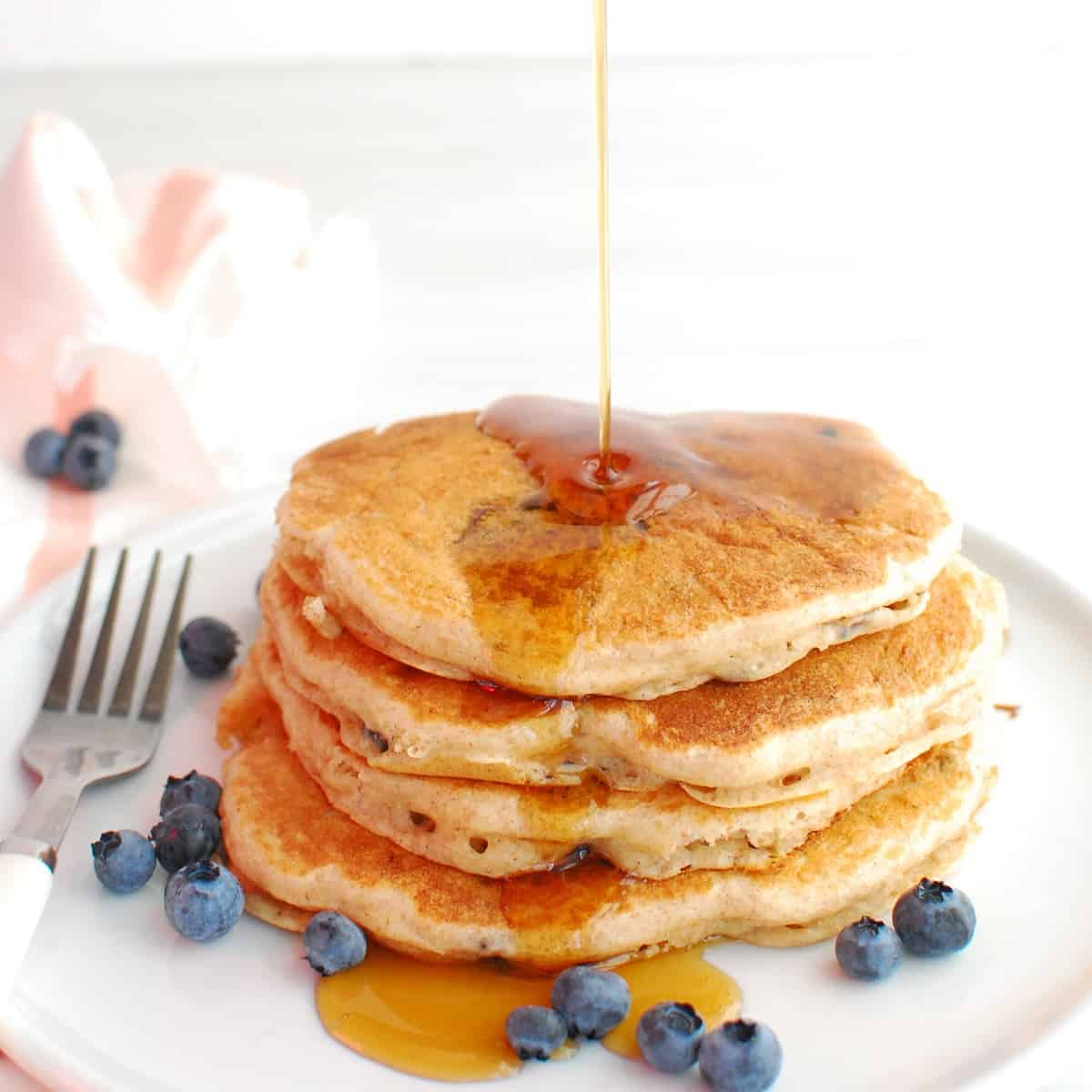 A stack of blueberry greek yogurt pancakes with maple syrup being drizzled on top.