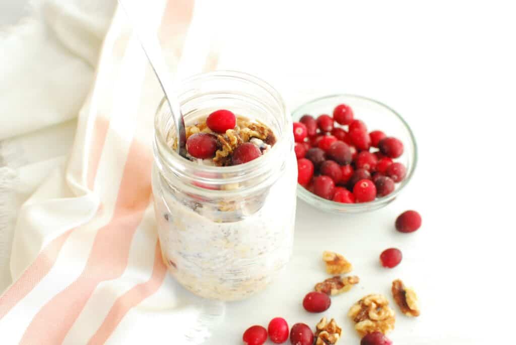 A mason jar with cranberry walnut overnight oats, next to a striped napkin.