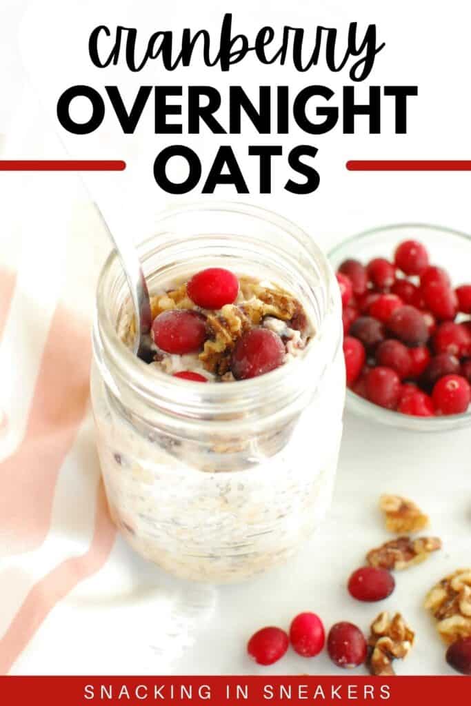 A mason jar with cranberry overnight oats, with a spoon in the jar, next to fresh cranberries and walnuts.