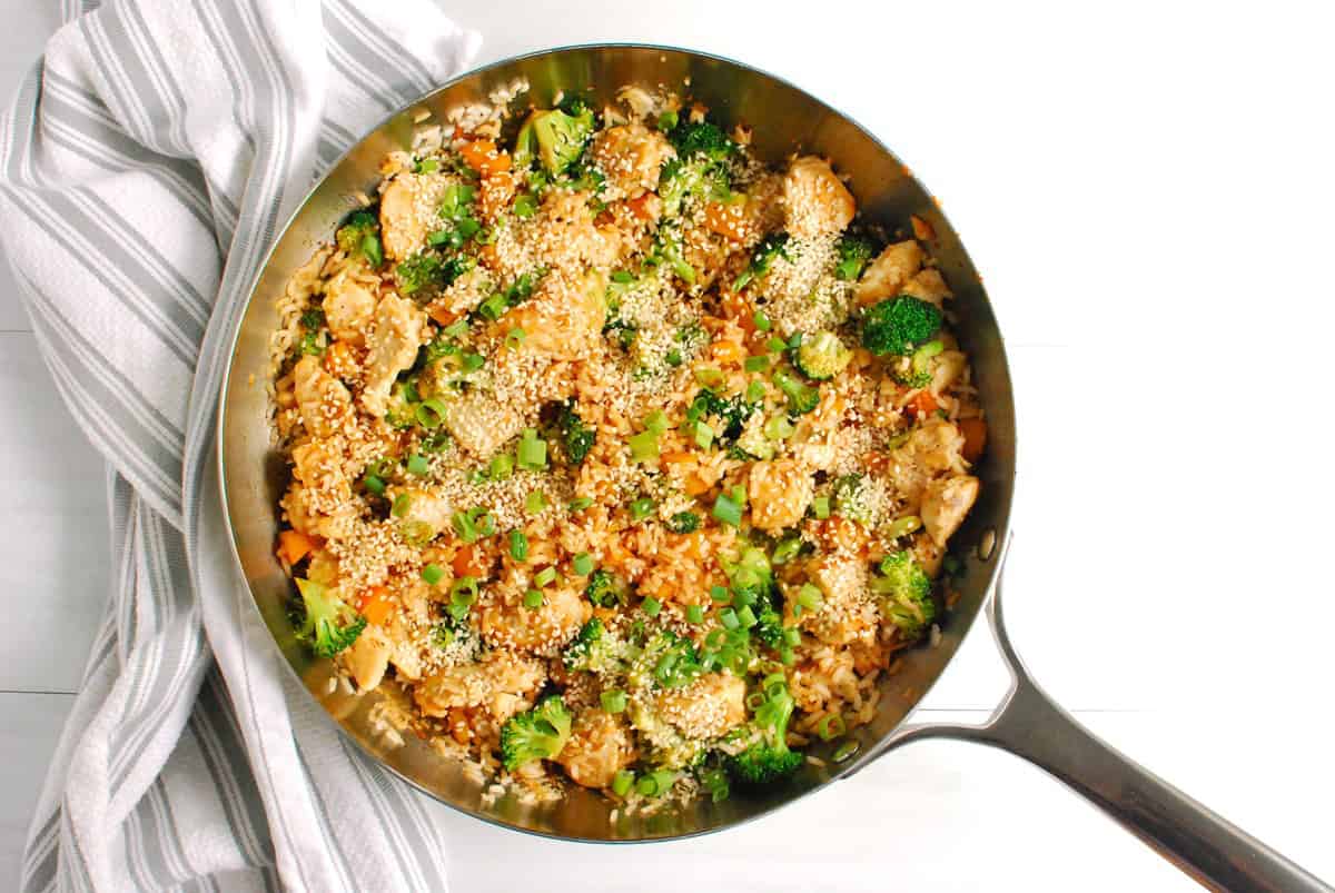 A large skillet with chicken, vegetable, and rice stir fry.