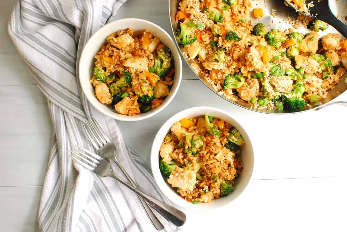 Two bowls of chicken stir fry next to a skillet with the rest of it.