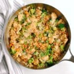 A skillet with chicken, vegetable, and rice stir fry, garnished with sesame seeds.