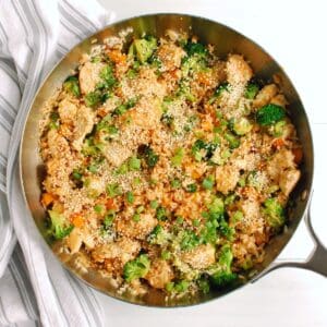 A skillet with chicken, vegetable, and rice stir fry, garnished with sesame seeds.