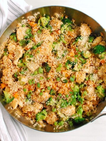 A skillet with chicken, vegetable, and rice stir fry, garnished with sesame seeds.