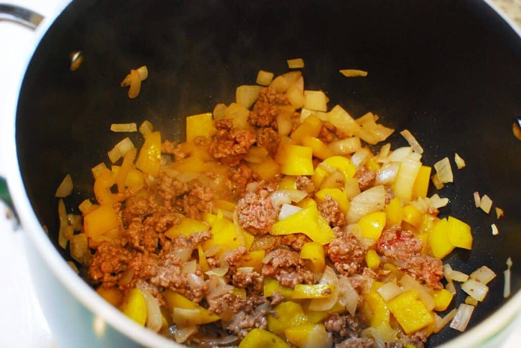 Ground beef sautéed with peppers and onions in a pot.
