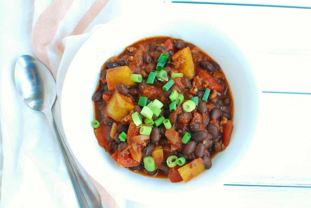 A bowl of chipotle chili topped with scallions next to a napkin.