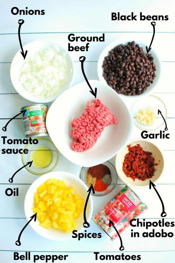 All of the ingredients, including ground beef, beans, pepper, onion, tomato sauce, garlic, oil, chipotle peppers, spices, and diced tomatoes.