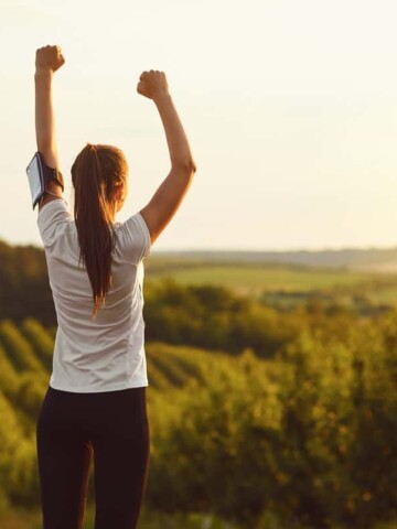 A runner raising her hands outside after a run, showing her love of running.