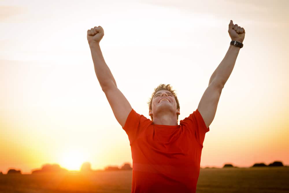 A male runner raising his hands in the air, happy after a run.