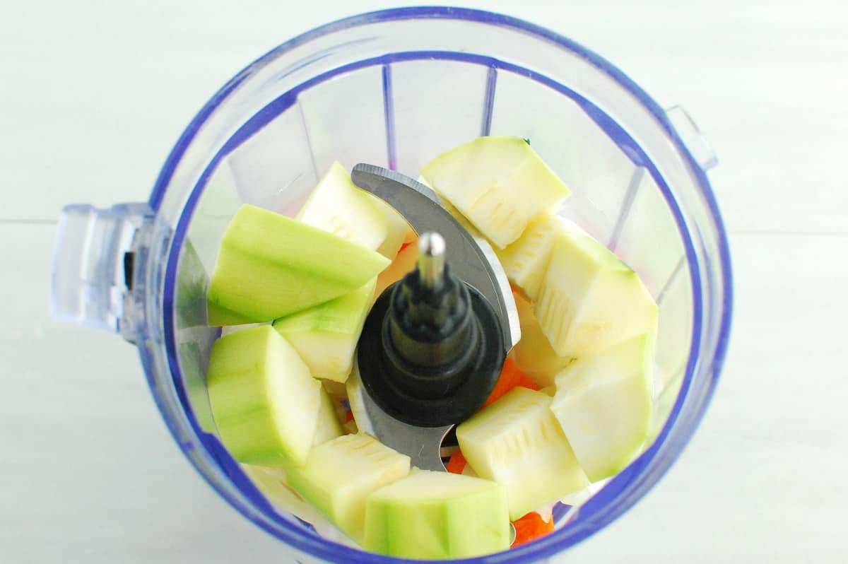 Zucchini, carrots, and onion in the bowl of a food processor.