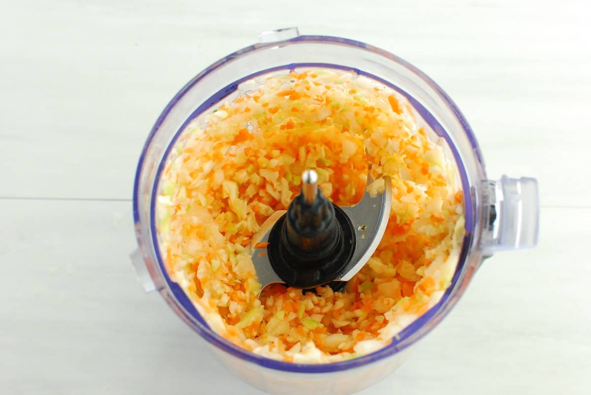 Shredded zucchini, carrot, and onion in the bowl of a food processor.