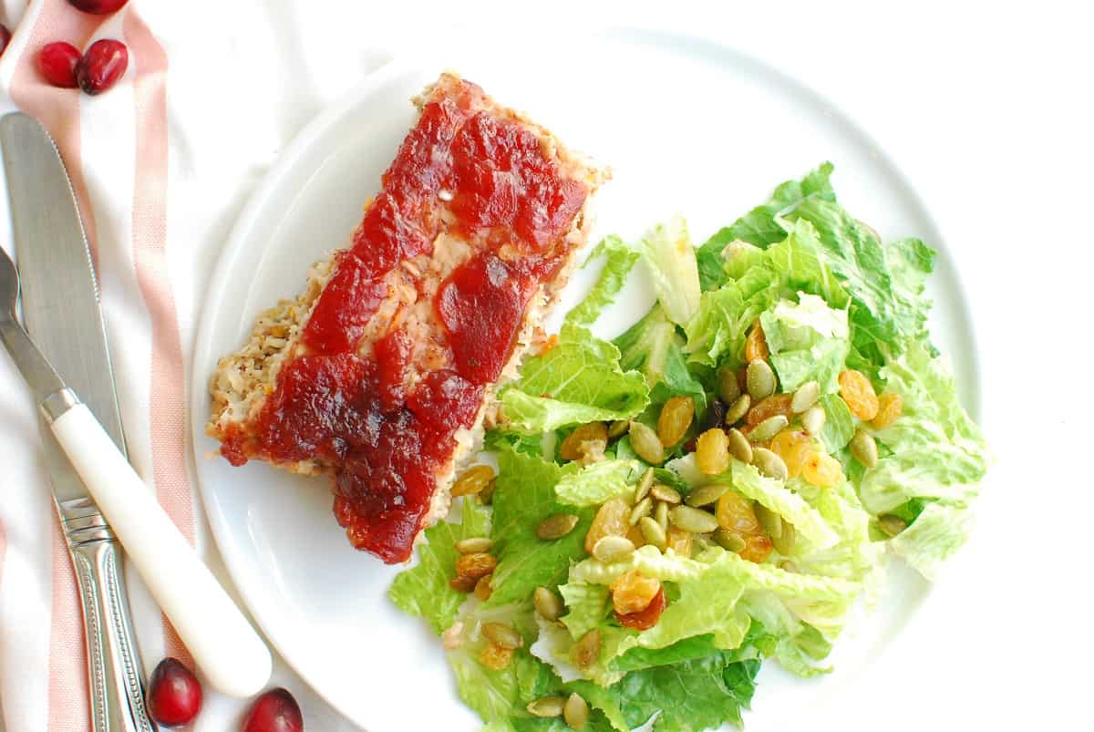 Meatloaf and salad on a white plate next to a napkin and fork.