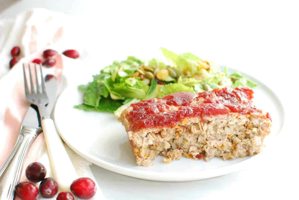 A slice of cranberry chicken meatloaf on a plate with salad.