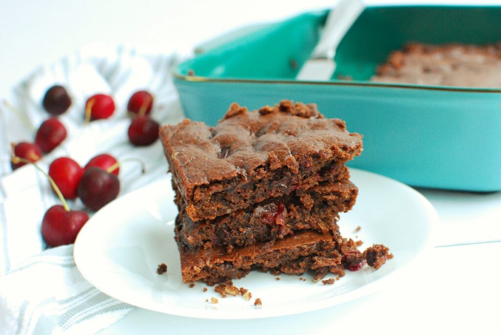 Three chocolate cherry brownies stacked on top of each other on a white plate.