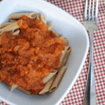 A bowl of pasta topped with vegetarian spaghetti sauce, next to a fork
