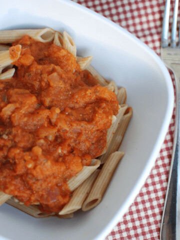 A bowl of pasta topped with vegetarian spaghetti sauce, next to a fork