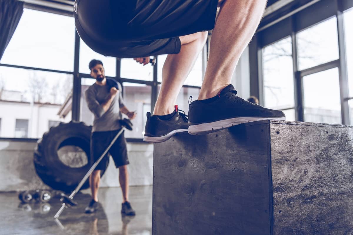 A man jumping on a box in a gym.