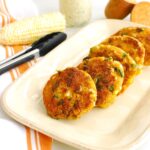 A platter of sweet potato corn fritters next to a pair of tongs.