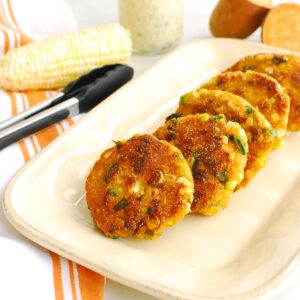 A platter of sweet potato corn fritters next to a pair of tongs.