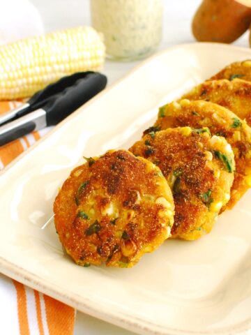 A platter of sweet potato corn fritters next to a pair of tongs.