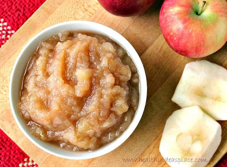 A bowl of homemade applesauce on a cutting board next to sliced apples.