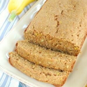 A loaf of summer squash bread with two slices cut out of it, next to a napkin.