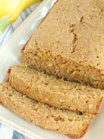 A loaf of summer squash bread with two slices cut out of it, next to a napkin.