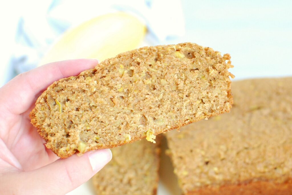 A woman's hand holding a slice of yellow squash bread.