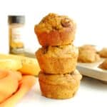 Three pumpkin banana chocolate chip muffins next to an orange napkin.