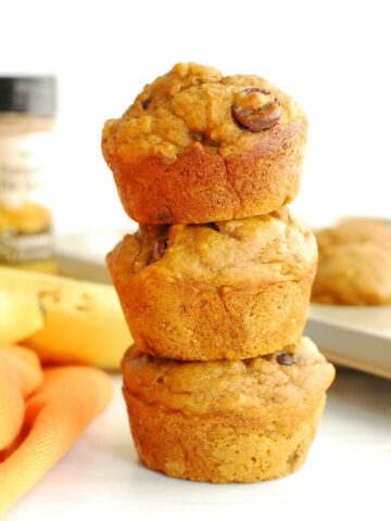 Three pumpkin banana chocolate chip muffins next to an orange napkin.