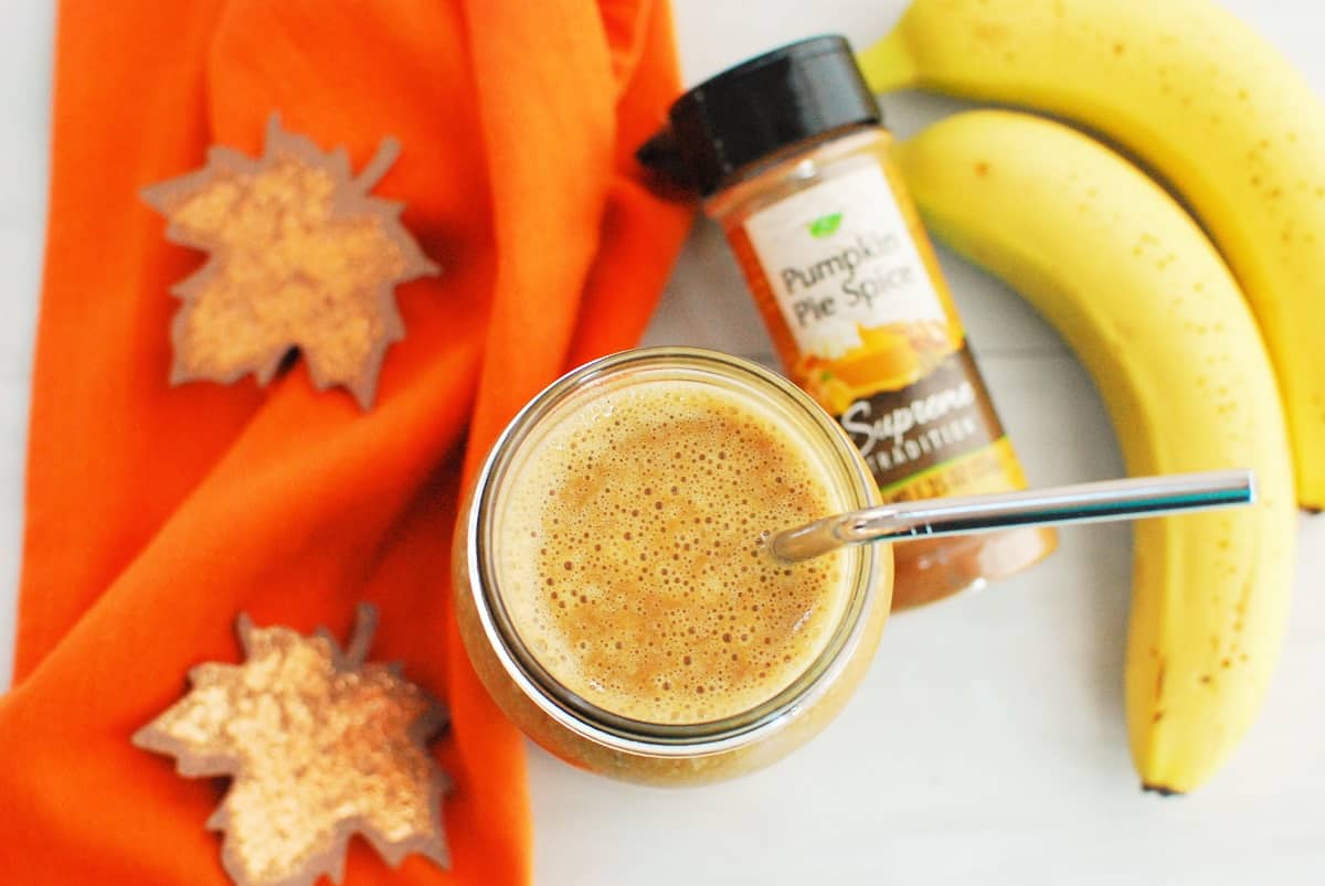Overhead view of a healthy pumpkin smoothie next to a napkin, pumpkin spice, and bananas.
