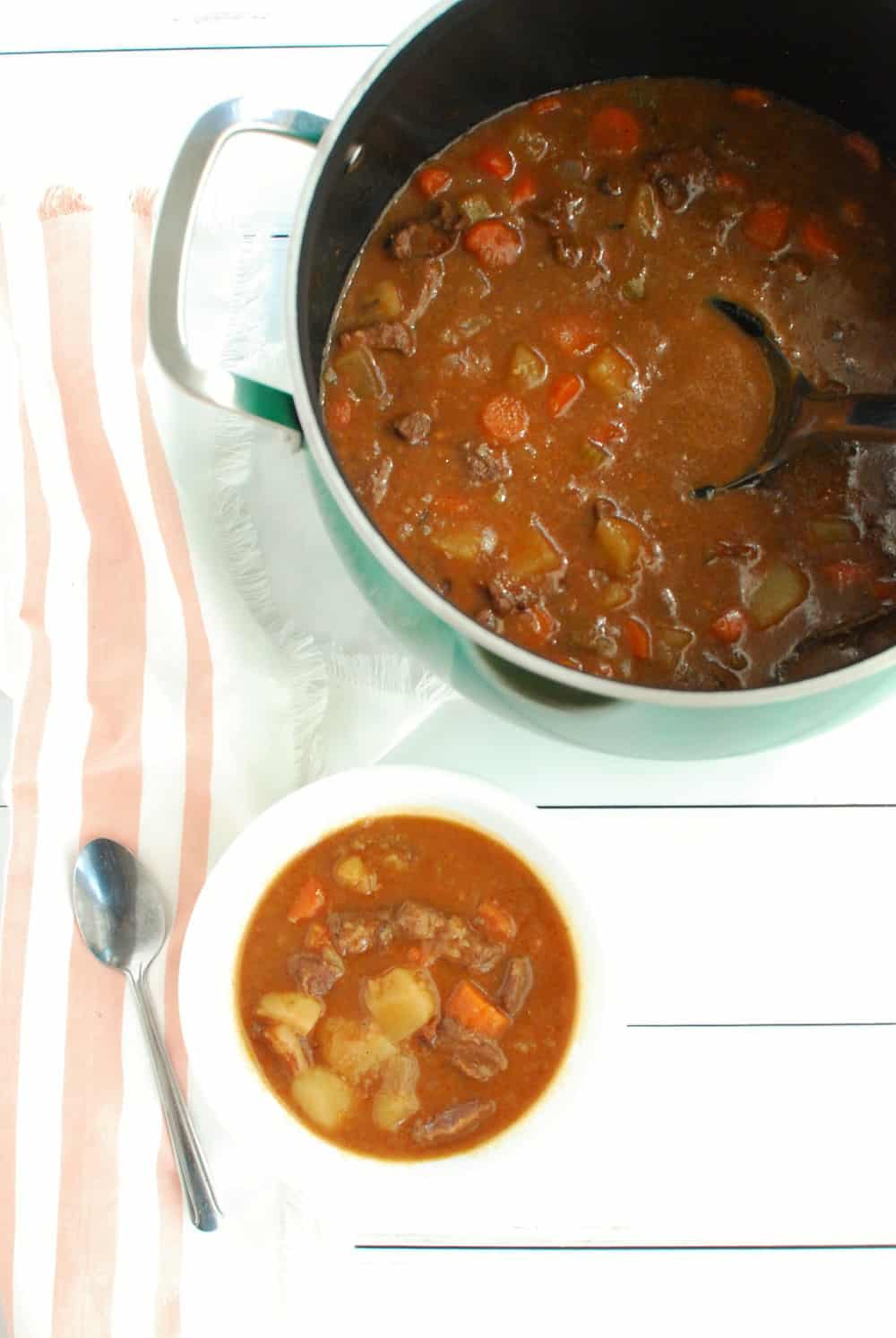 A bowl of beef stew next to a pot full of it.