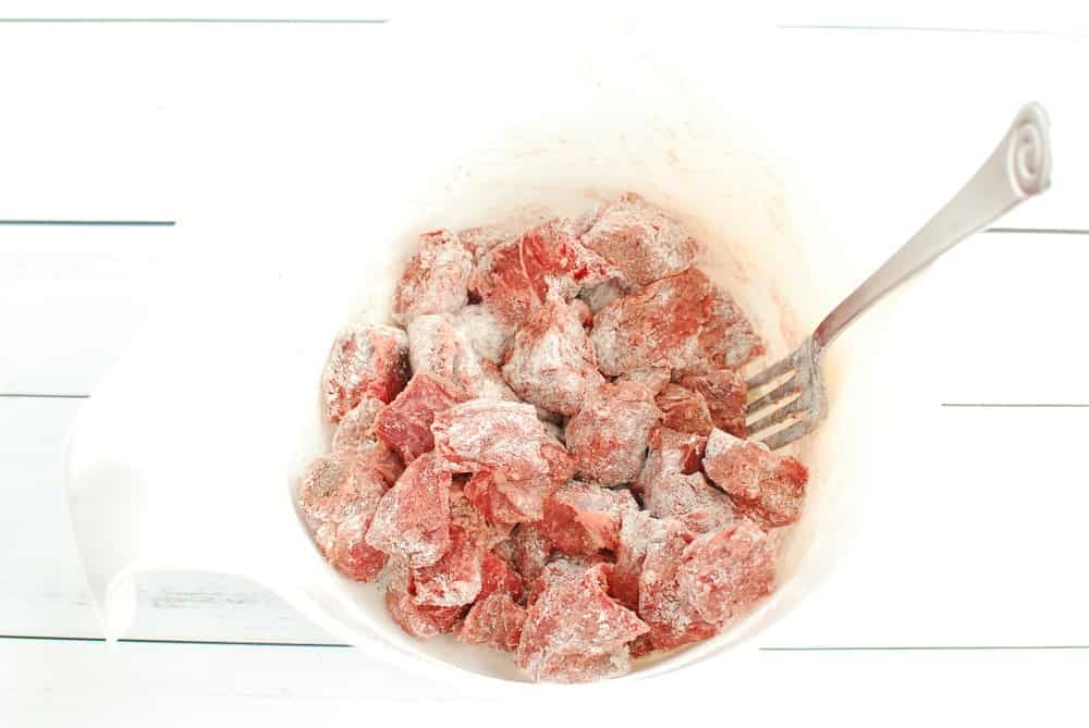 Beef tossed in flour, salt, and pepper, in a bowl.