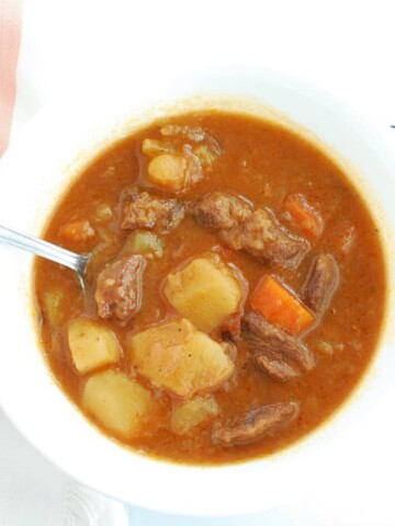 An overhead shot of a bowl of beef stew next to a pink striped napkin.