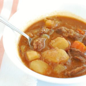 A bowl of stovetop beef stew with a spoon in it.