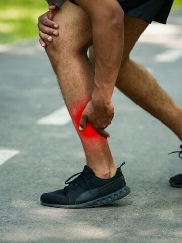 A runner grasping his calf on the road as he experiences an injury.