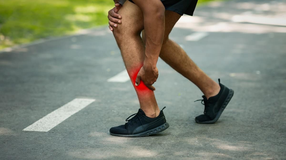 A runner grasping his calf on the road as he experiences an injury.