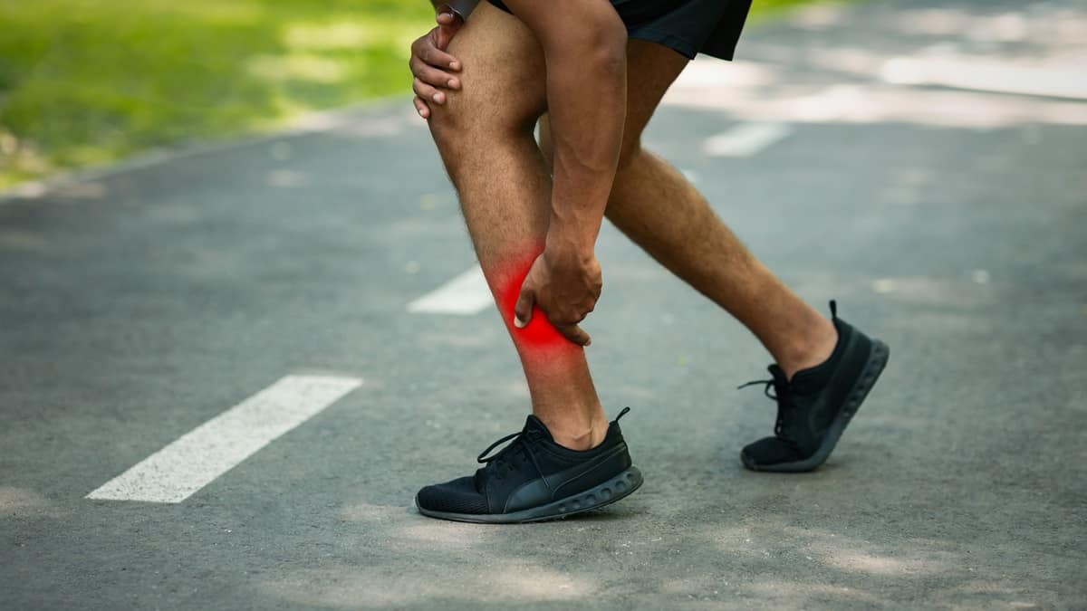 A runner grasping his calf on the road as he experiences an injury.