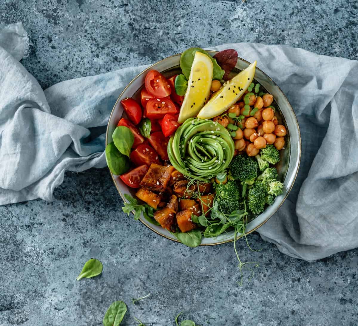 A healthy bowl of food with sweet potatoes, tomato, chickpeas, broccoli, and avocado.