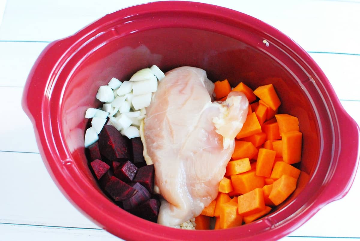 A crockpot filled with onion, beets, chicken, and butternut squash.